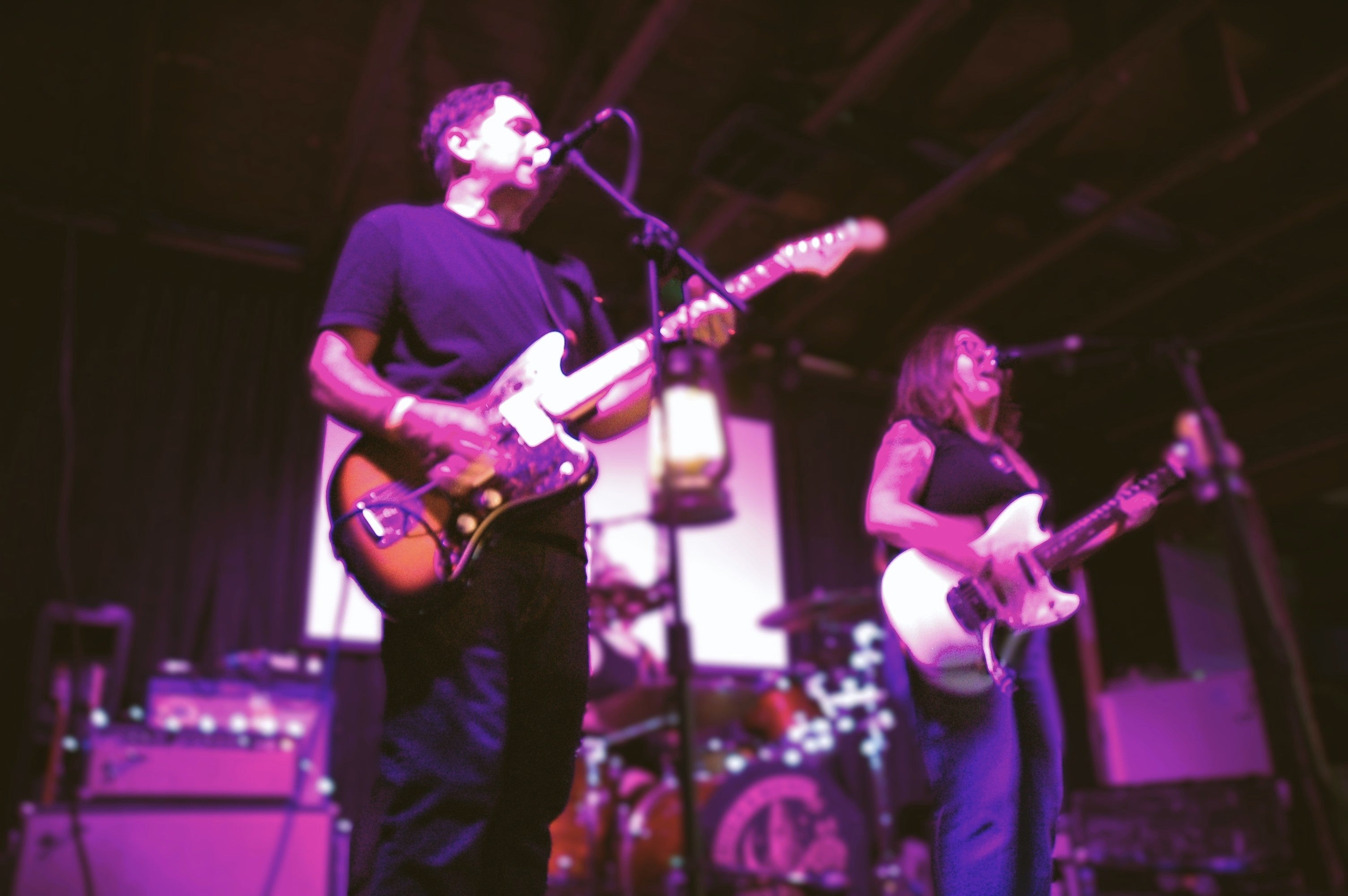 Two musicians playing guitar on stage with a purple hue